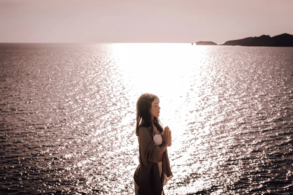 Een vrouw met gevouwen handen in het tegenlicht van de glinsterende zee