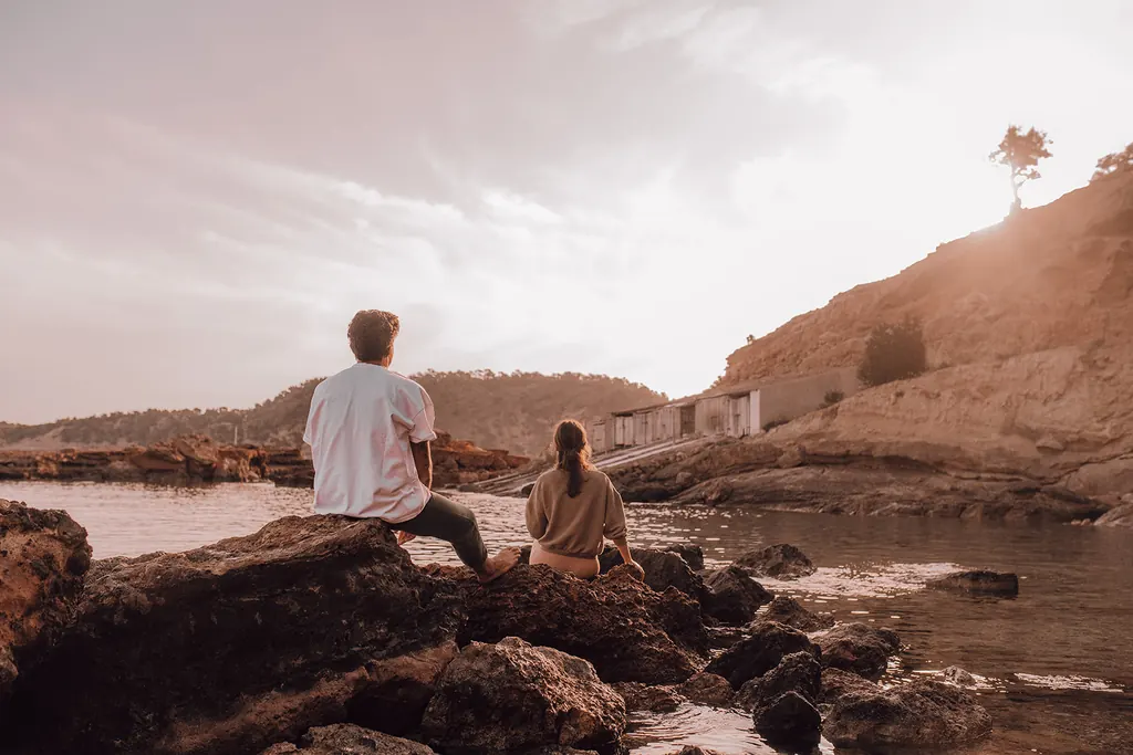 Twee mensen zitten zwijgend op de rotsen aan de baai in het ochtendlicht