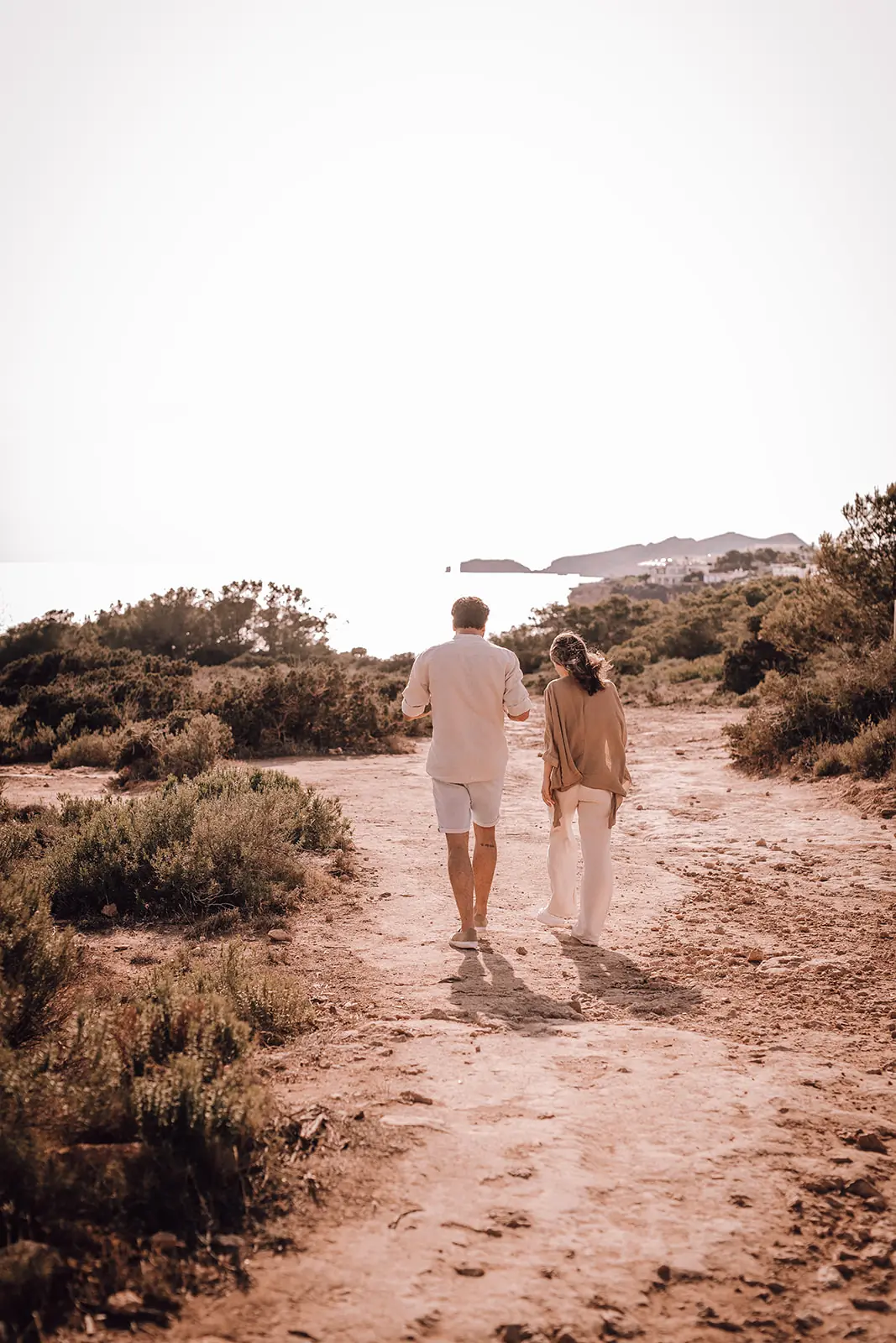 Twee mensen wandelen over een zandpad richting zee