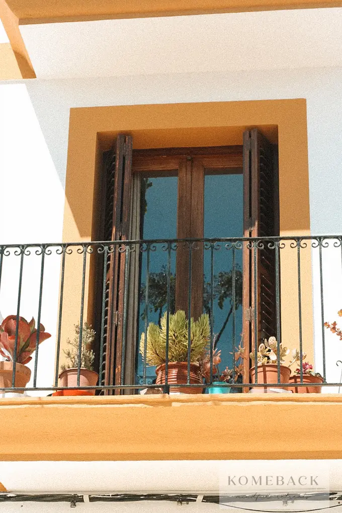 Een balkon met planten tegen een gele gevel