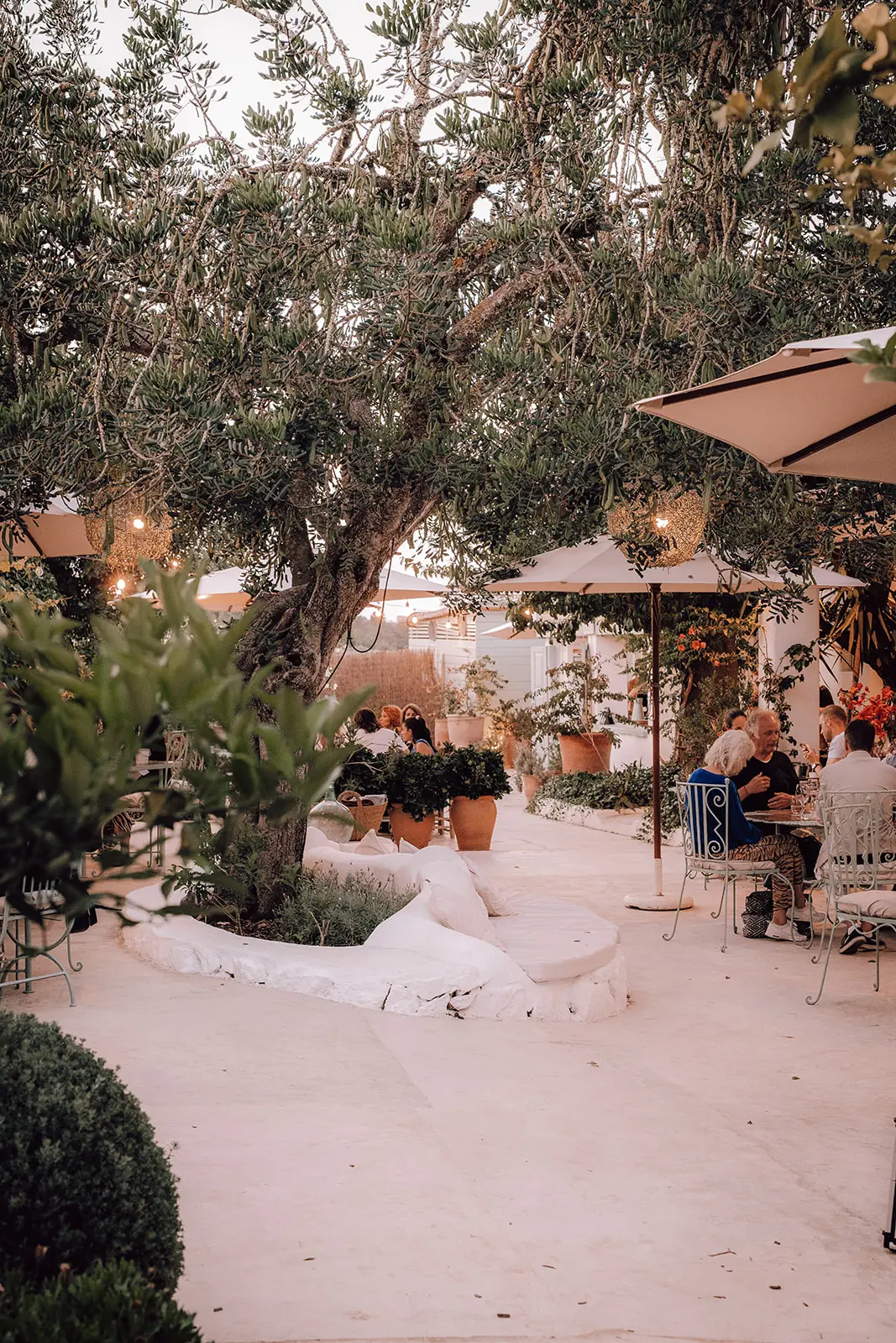 Een tuinrestaurant met parasols en mensen aan tafel in de avond